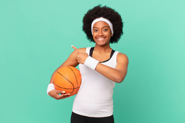 afro woman looking excited and surprised pointing to the side and upwards to copy space. basketball concept - Zdjęcie, obraz