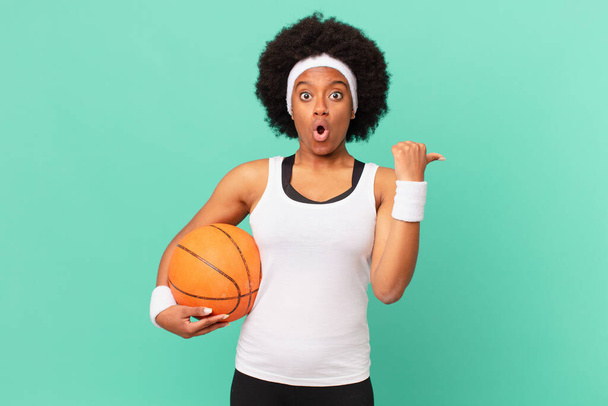 afro woman looking astonished in disbelief, pointing at object on the side and saying wow, unbelievable. basketball concept - Zdjęcie, obraz