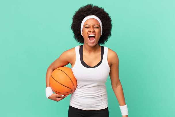 afro woman shouting aggressively, looking very angry, frustrated, outraged or annoyed, screaming no. basketball concept - Foto, afbeelding