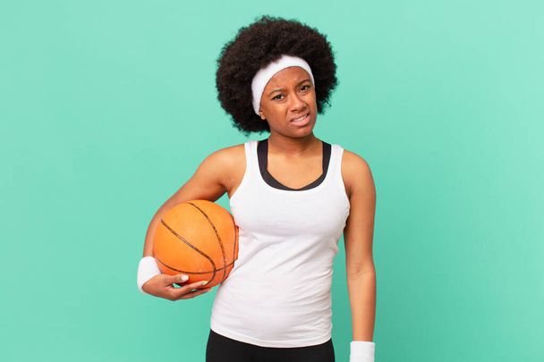 afro woman feeling puzzled and confused, with a dumb, stunned expression looking at something unexpected. basketball concept - Foto, afbeelding