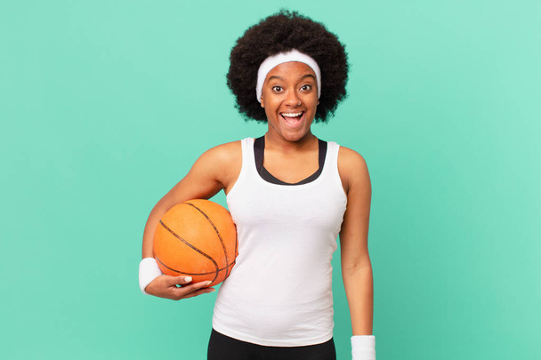 afro женщина выглядит счастливым и приятно удивлен, взволнован с очаровательным и шокированным выражением лица. баскетбол - Фото, изображение