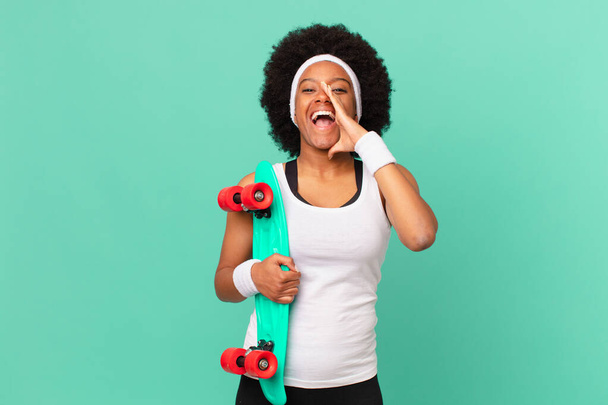 afro woman feeling happy, excited and positive, giving a big shout out with hands next to mouth, calling out. skateboard concept - Foto, Imagen