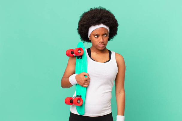 afro woman feeling sad, upset or angry and looking to the side with a negative attitude, frowning in disagreement. skateboard concept - Fotó, kép
