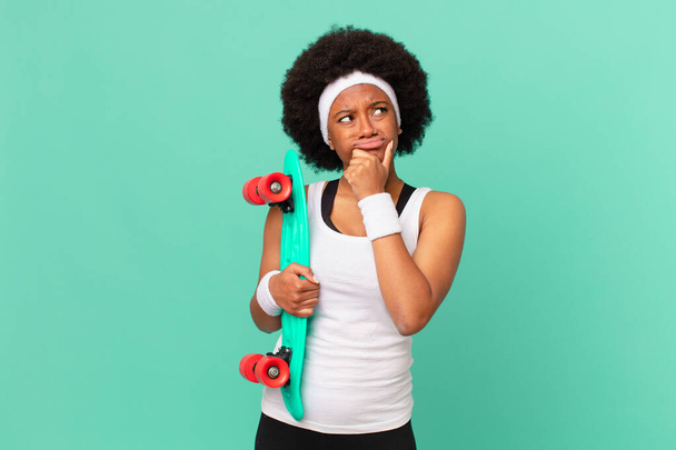 afro woman thinking, feeling doubtful and confused, with different options, wondering which decision to make. skateboard concept - 写真・画像