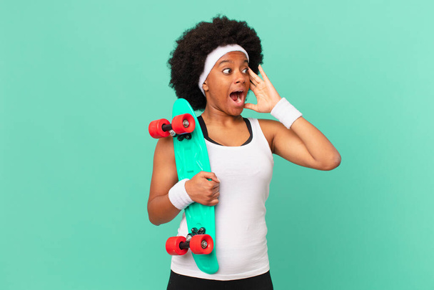 afro woman feeling happy, excited and surprised, looking to the side with both hands on face. skateboard concept - Foto, Imagen