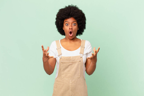 afro woman open-mouthed and amazed, shocked and astonished with an unbelievable surprise chef concept - Foto, Imagem