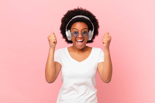 afro woman feeling shocked, excited and happy, laughing and celebrating success, saying wow!. music concept - 写真・画像