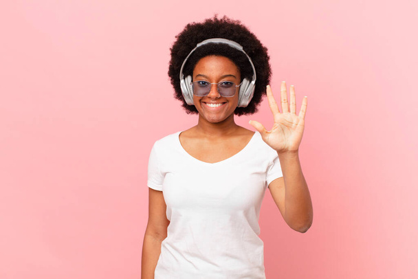 afro woman smiling and looking friendly, showing number five or fifth with hand forward, counting down. music concept - 写真・画像