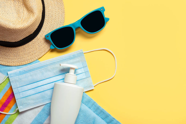 Protective surgical mask with sunglasses,hat and plastic bottle of sunscreen with copy space on a yellow background.Summer concept with covid-19 - Photo, Image