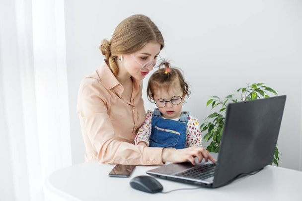 Gyönyörű üzletasszony dolgozik a számítógépén, miközben időt tölt az aranyos kislányával - Fotó, kép