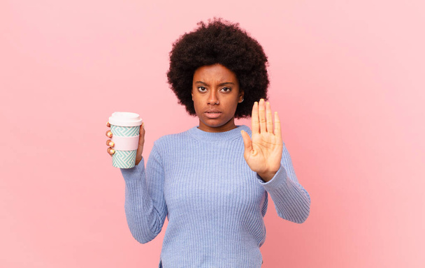 afro woman looking serious, stern, displeased and angry showing open palm making stop gesture. coffee concept - Foto, Bild