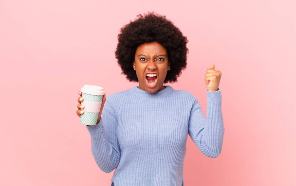 afro woman shouting aggressively with an angry expression or with fists clenched celebrating success. coffee concept - Fotografie, Obrázek