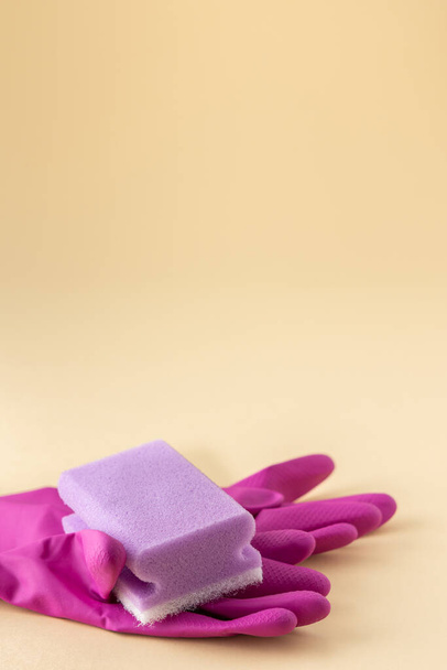 Gants en caoutchouc rose et éponge lave-vaisselle violette sur fond beige neutre, concept de nettoyage - Photo, image