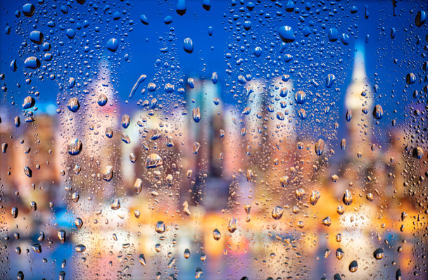 Hermosa vista conceptual del paisaje de la ciudad a través de una ventana de cristal con gotas de lluvia. Lluvia en vista nocturna urbana de la ciudad. - Foto, imagen