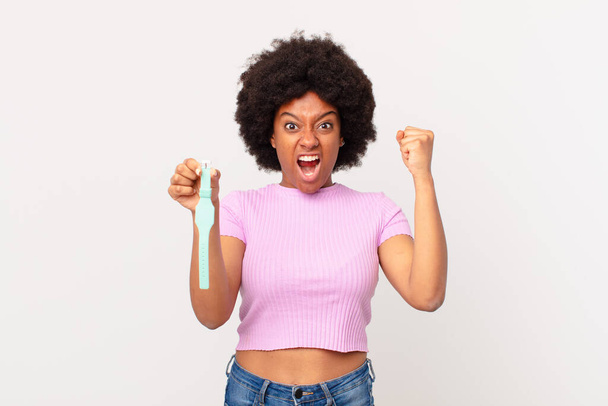 afro woman shouting aggressively with an angry expression or with fists clenched celebrating success watch concept - Foto, Imagem