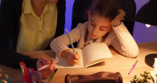 Žena pomáhá své malé dceři s domácím úkolem pozdě večer - Záběry, video