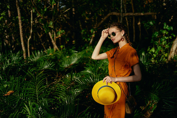 Sarı şapkalı ve elbiseli bir kadın ormanda dolaşır. - Fotoğraf, Görsel