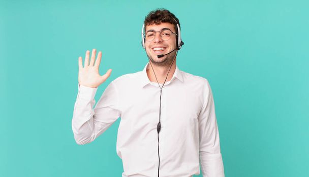 telemarketer smiling happily and cheerfully, waving hand, welcoming and greeting you, or saying goodbye - Foto, afbeelding