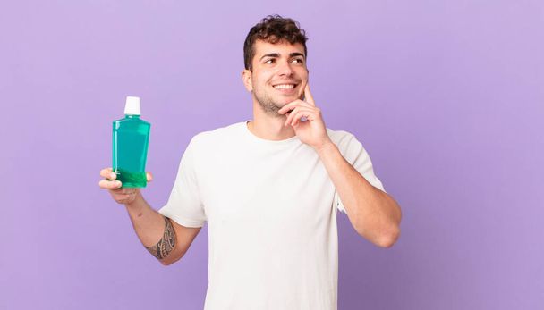 man with mouthwash smiling happily and daydreaming or doubting, looking to the side - Foto, imagen