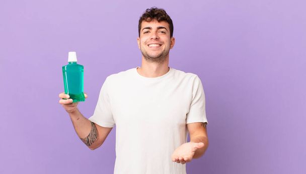 man with mouthwash smiling happily with friendly, confident, positive look, offering and showing an object or concept - Zdjęcie, obraz