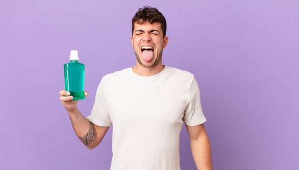 man with mouthwash with cheerful, carefree, rebellious attitude, joking and sticking tongue out, having fun - Photo, Image