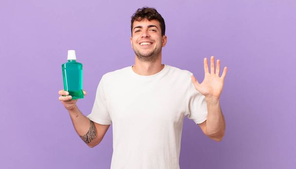man with mouthwash smiling happily and cheerfully, waving hand, welcoming and greeting you, or saying goodbye - Foto, Bild
