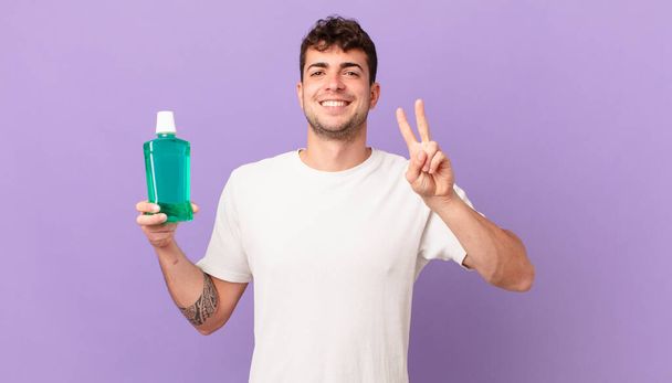 man with mouthwash smiling and looking friendly, showing number two or second with hand forward, counting down - Zdjęcie, obraz