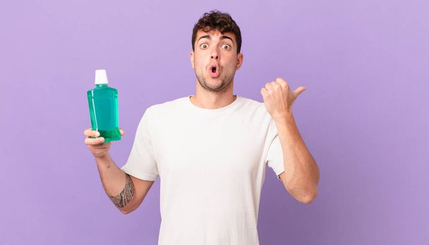 man with mouthwash looking astonished in disbelief, pointing at object on the side and saying wow, unbelievable - Foto, Imagen
