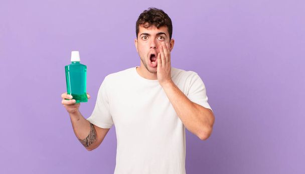 man with mouthwash feeling shocked and scared, looking terrified with open mouth and hands on cheeks - Fotoğraf, Görsel