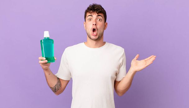 man with mouthwash looking surprised and shocked, with jaw dropped holding an object with an open hand on the side - Fotografie, Obrázek