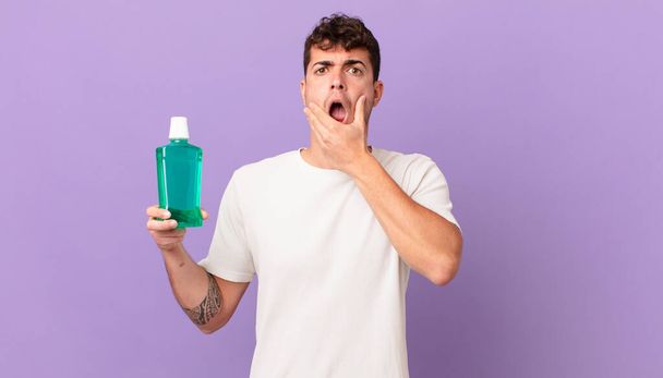 man with mouthwash with mouth and eyes wide open and hand on chin, feeling unpleasantly shocked, saying what or wow - Фото, изображение