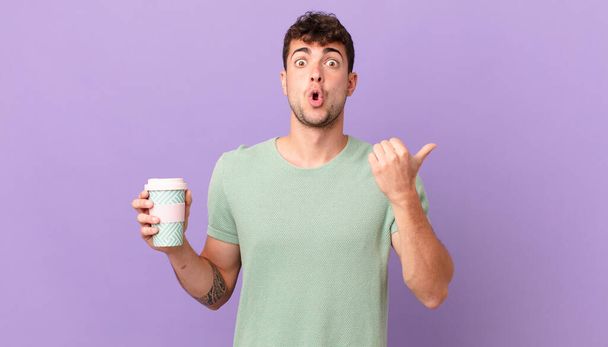 man with coffee looking astonished in disbelief, pointing at object on the side and saying wow, unbelievable - Photo, Image