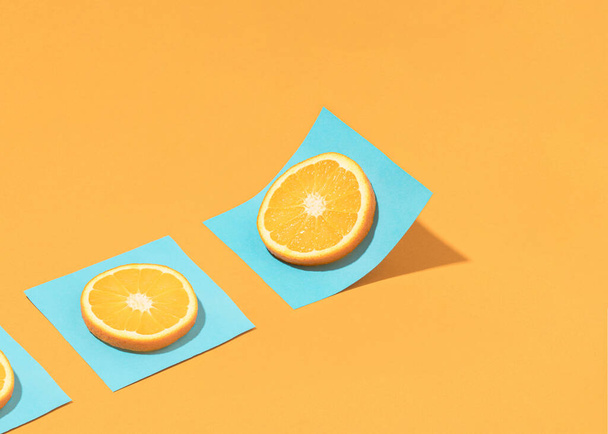 Модна літня композиція з цитрусовими фруктовими скибочками на яскраво-блакитному паперовому листі над сонячним помаранчевим столом. Мінімальний фон органічної їжі
. - Фото, зображення