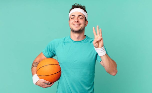 homem fitness sorrindo e olhando amigável, mostrando o número três ou terceiro com a mão para a frente, contando para baixo - Foto, Imagem