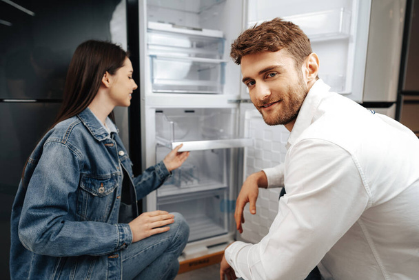 Young couple selecting new refrigerator in household appliance store - Foto, Imagen