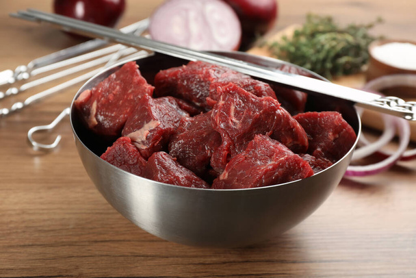 Metal skewers and bowl with raw meat on wooden table - Photo, image