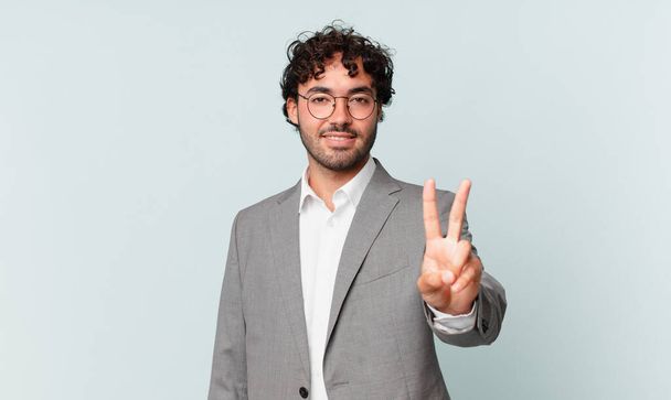 hispanic businessman smiling and looking friendly, showing number two or second with hand forward, counting down - Foto, afbeelding