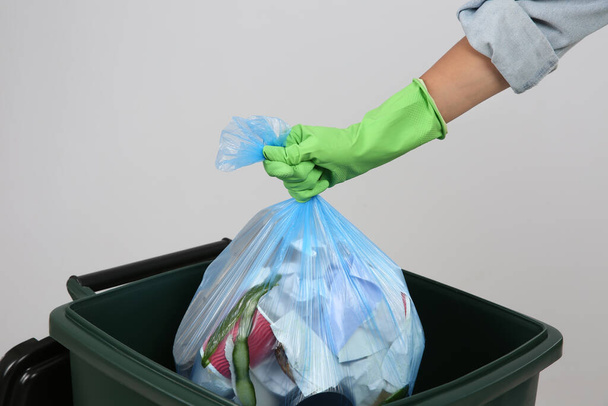 Woman throwing garbage bag into bin on light background, closeup - Photo, Image