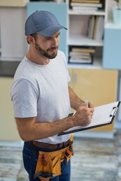 Quality service. Professional young repairman making notes on clipboard while standing indoors - Photo, Image