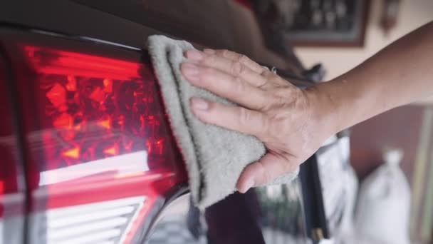 Mužská ruka za použití mokré ručníkové látky setře prach z jeho automobilové části. čištění zadní části vozidla znečištěný povrch, leštidlo na leštění aut, aktivita doma, údržba vozidla, reflexe záběru zblízka - Záběry, video