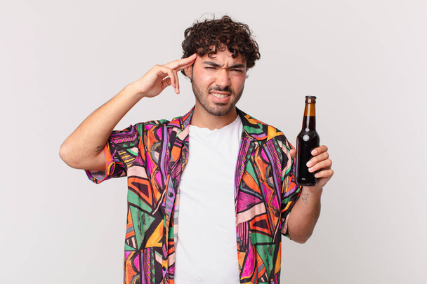 hispanic man with beer feeling confused and puzzled, showing you are insane, crazy or out of your mind - Foto, immagini