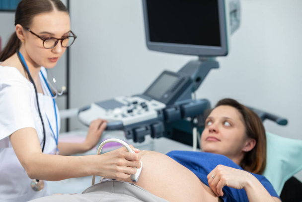 A lady doctor checks the abdomen of a pregnant patient with an ultrasound. Gynecology office. - Photo, image