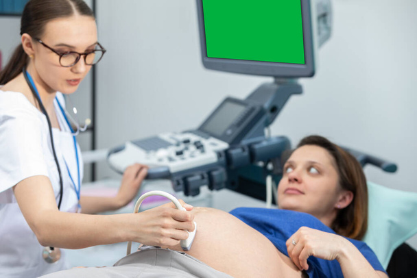 A lady doctor checks the abdomen of a pregnant patient with an ultrasound. Gynaecology office. Green screen. - Foto, immagini