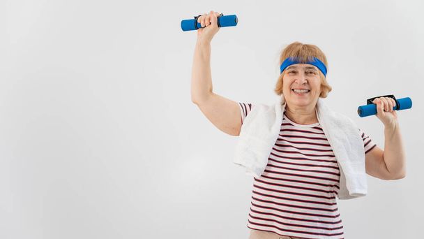 An elderly woman with a blue bandage on her head trains with dumbbells on a white background - Fotografie, Obrázek