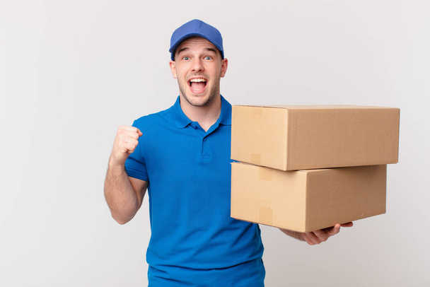 package deliver man feeling shocked, excited and happy, laughing and celebrating success, saying wow! - Photo, image