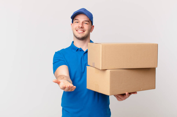 package deliver man smiling happily with friendly, confident, positive look, offering and showing an object or concept - Foto, Imagem