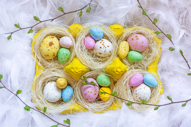 Зі святом Великодня. Цукерки у вигляді яєць в гніздах на тлі пір'я
 - Фото, зображення