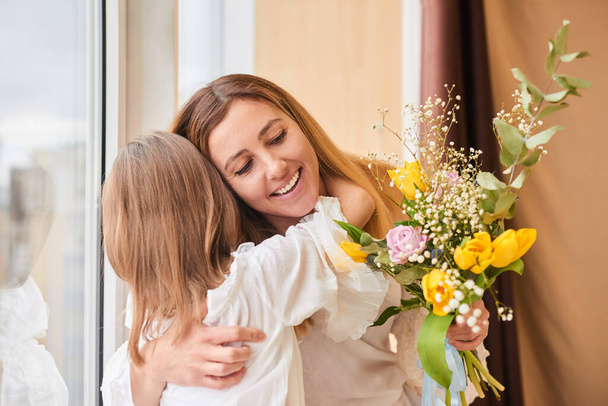 anya és lánya ölelés virágokkal - család, gyermek, nyaralás és party koncepció - Fotó, kép