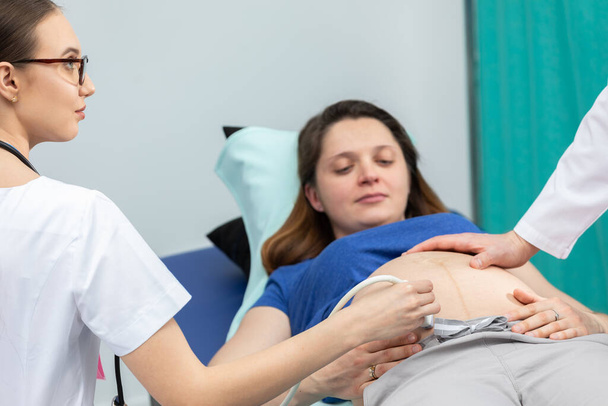 Медсестра оглядає живіт ультразвуковим апаратом, а лікар м'яко торкається вагітних пацієнтів живота
. - Фото, зображення