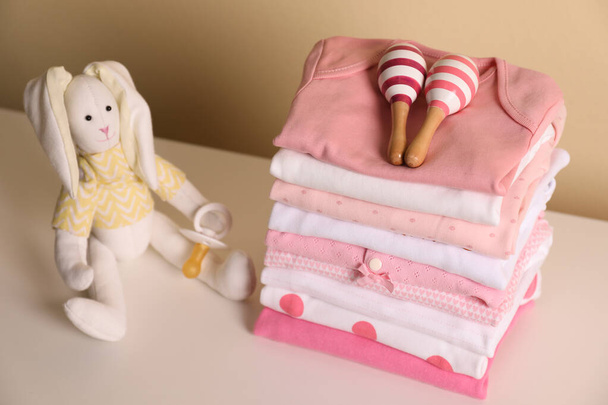 Stack of baby girl's clothes, rattles, pacifier and toy bunny on white table - Fotó, kép